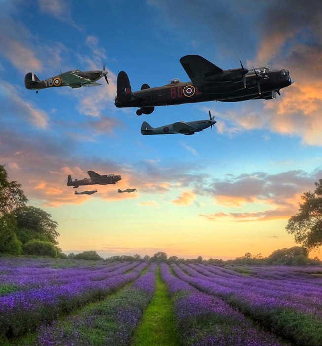 World War 2 Lancaster, Spitfire and Hurricane planes flying over a field with the sun low in the sky